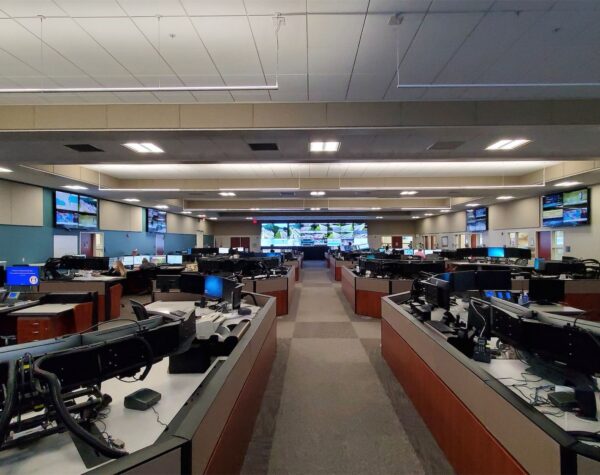 Interior of a modern transportation operations center office featuring workstations, large display screens, and staff monitoring traffic systems in real time.